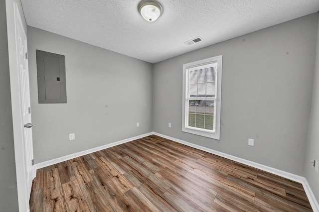 empty room featuring electric panel, wood-type flooring, and a textured ceiling