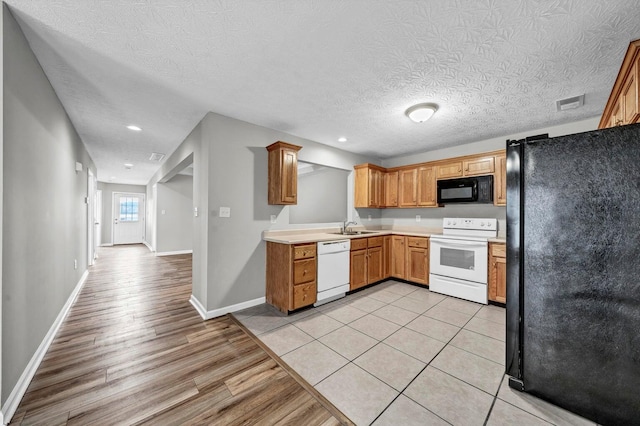 kitchen featuring black appliances, sink, light wood-type flooring, and a textured ceiling