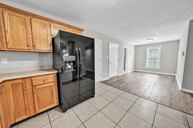 kitchen featuring black refrigerator with ice dispenser, a textured ceiling, and light hardwood / wood-style flooring