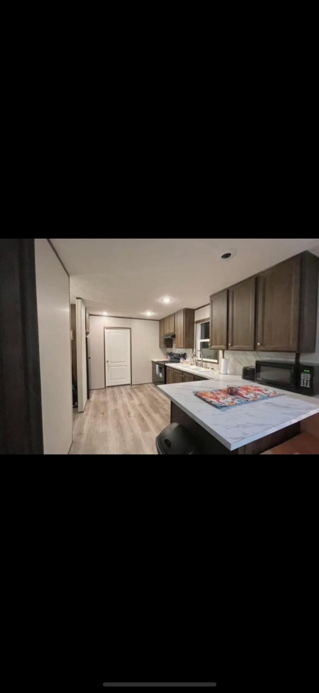 kitchen with tasteful backsplash, dark brown cabinets, a breakfast bar, kitchen peninsula, and light hardwood / wood-style flooring