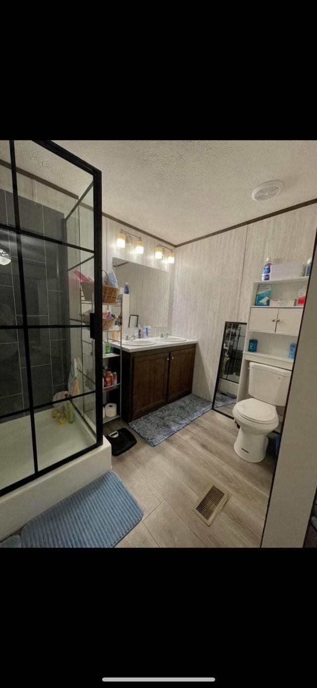 bathroom with toilet, a shower with door, hardwood / wood-style floors, a textured ceiling, and vanity