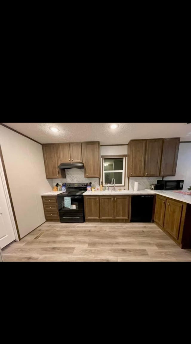 kitchen with black appliances, sink, light hardwood / wood-style floors, and a textured ceiling