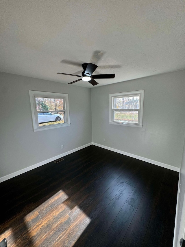 empty room featuring a textured ceiling, a healthy amount of sunlight, dark hardwood / wood-style floors, and ceiling fan