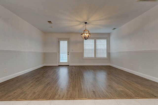 empty room featuring wood-type flooring and a chandelier