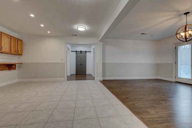 unfurnished room featuring a barn door, a chandelier, and light wood-type flooring