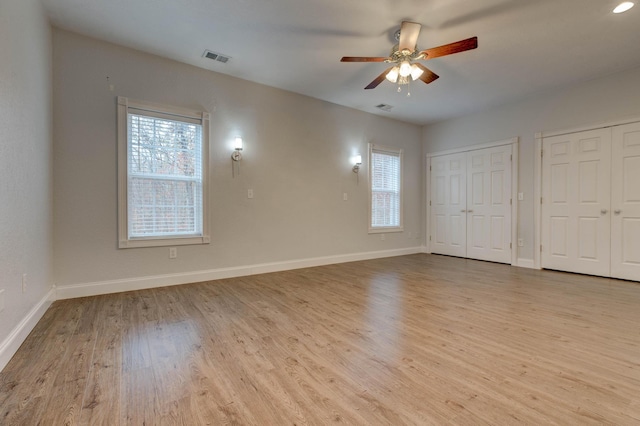 unfurnished bedroom featuring light wood-type flooring, multiple windows, multiple closets, and ceiling fan