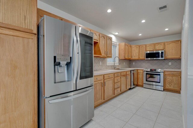 kitchen featuring backsplash, sink, light tile patterned floors, and appliances with stainless steel finishes