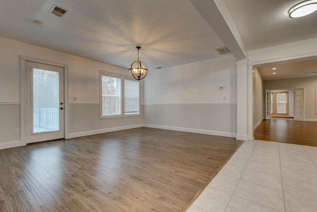 unfurnished room with a textured ceiling, light hardwood / wood-style floors, ornate columns, and a notable chandelier