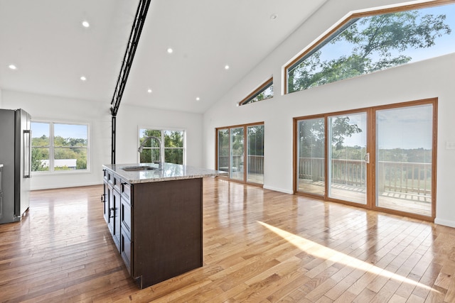 kitchen featuring high vaulted ceiling, sink, stainless steel fridge, light stone countertops, and light hardwood / wood-style floors