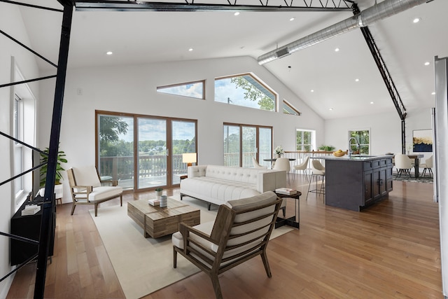 living room with light hardwood / wood-style floors, sink, and high vaulted ceiling