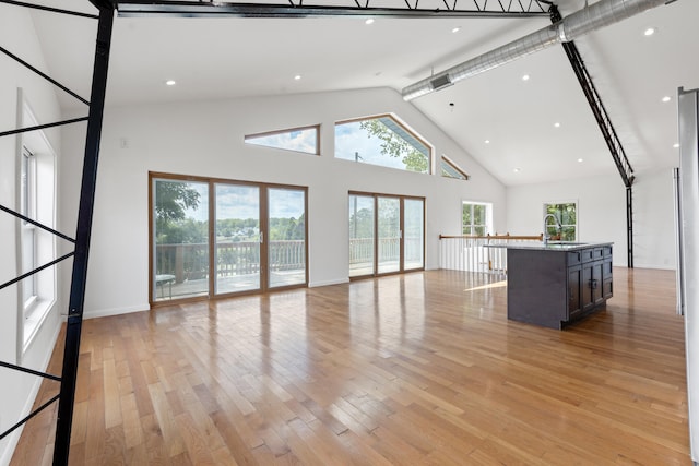 unfurnished living room with beam ceiling, light wood-type flooring, high vaulted ceiling, and sink