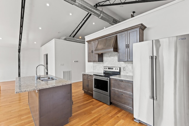 kitchen featuring a kitchen island with sink, sink, light stone countertops, appliances with stainless steel finishes, and light hardwood / wood-style floors