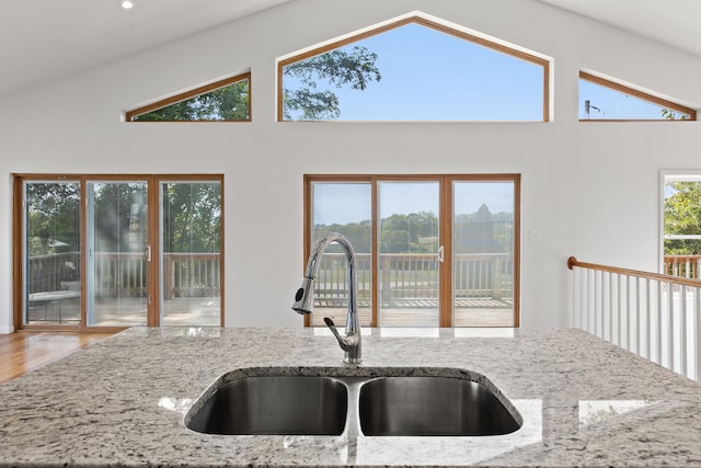 kitchen featuring light stone countertops, hardwood / wood-style flooring, high vaulted ceiling, and sink