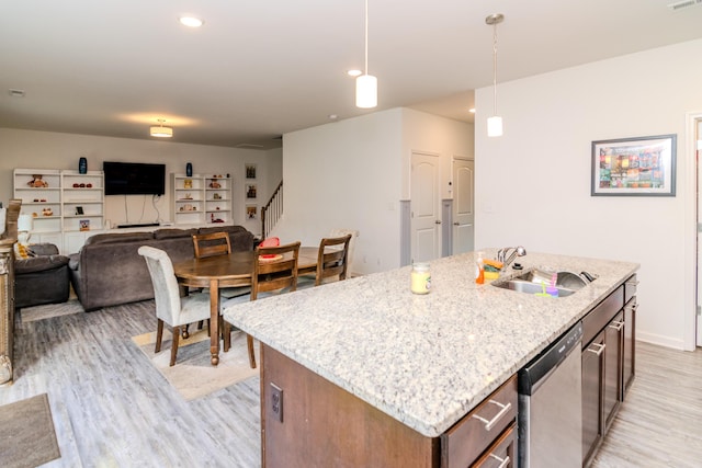 kitchen featuring sink, a kitchen island with sink, stainless steel dishwasher, pendant lighting, and light hardwood / wood-style flooring