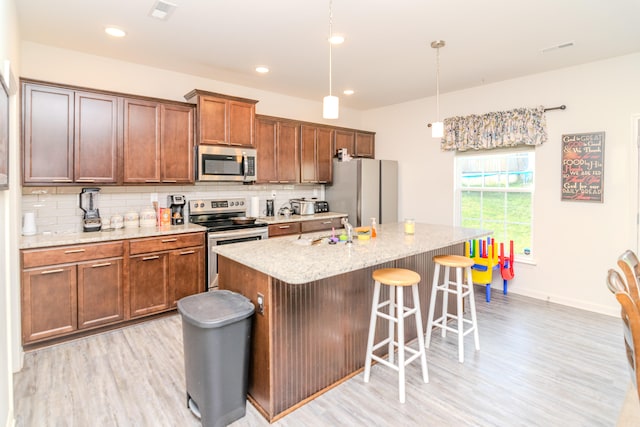 kitchen with stainless steel appliances, a kitchen island with sink, pendant lighting, and backsplash