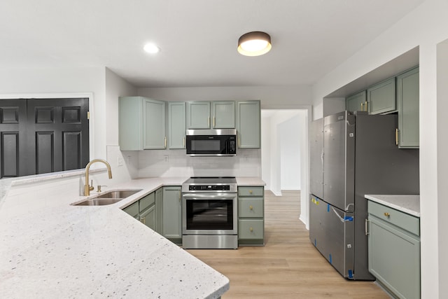 kitchen featuring stainless steel appliances, green cabinets, sink, tasteful backsplash, and light wood-type flooring