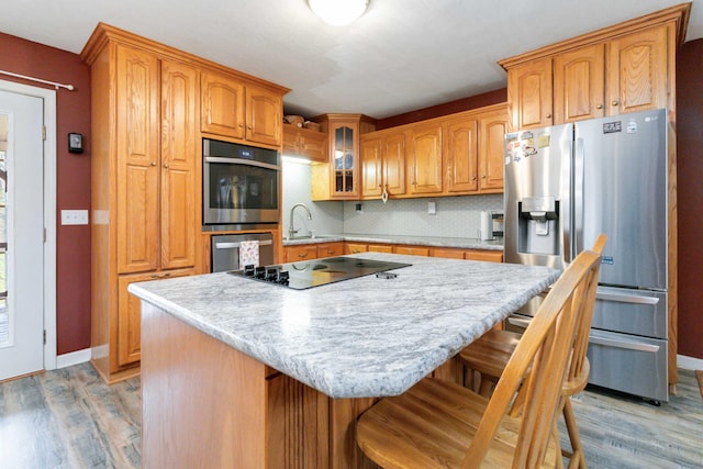 kitchen featuring light hardwood / wood-style floors, appliances with stainless steel finishes, tasteful backsplash, a breakfast bar area, and a center island