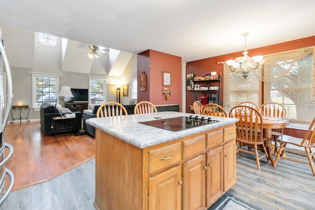 kitchen with ceiling fan with notable chandelier, black electric cooktop, a center island, light wood-type flooring, and decorative light fixtures