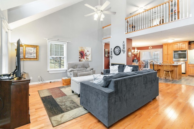 living room featuring high vaulted ceiling, light wood-type flooring, and ceiling fan with notable chandelier