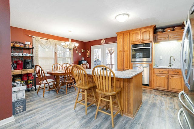 kitchen with wood-type flooring, stainless steel appliances, pendant lighting, an inviting chandelier, and a breakfast bar