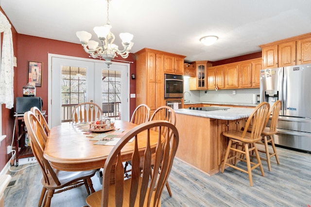 kitchen featuring stainless steel appliances, light hardwood / wood-style floors, hanging light fixtures, a notable chandelier, and french doors