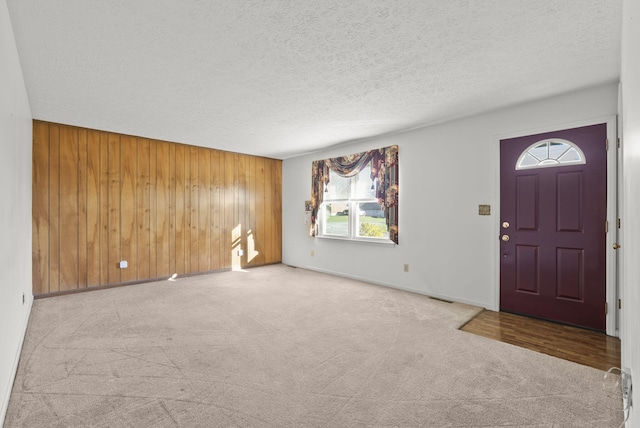 entrance foyer featuring light carpet, a textured ceiling, and wood walls