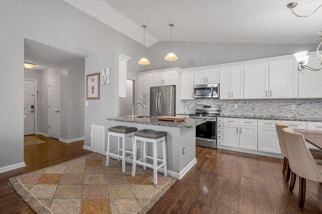 kitchen with appliances with stainless steel finishes, stone counters, lofted ceiling, white cabinets, and dark wood-type flooring