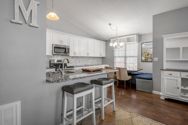 kitchen featuring stone countertops, appliances with stainless steel finishes, a breakfast bar area, lofted ceiling, and white cabinets