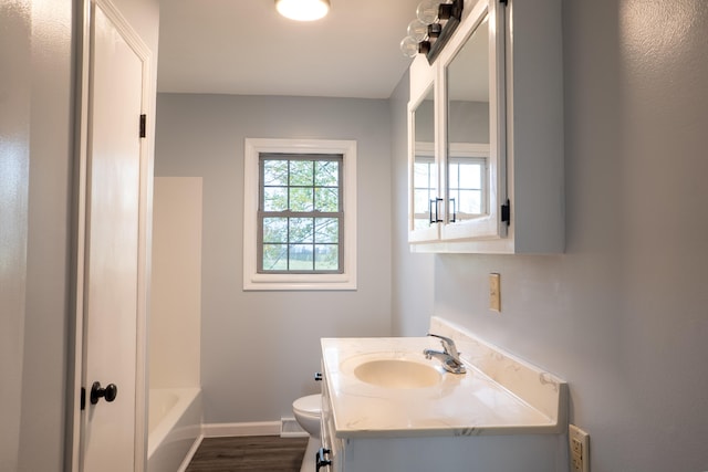 bathroom with a bath, hardwood / wood-style flooring, vanity, and toilet