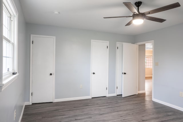 unfurnished bedroom featuring ceiling fan, multiple windows, and dark hardwood / wood-style flooring