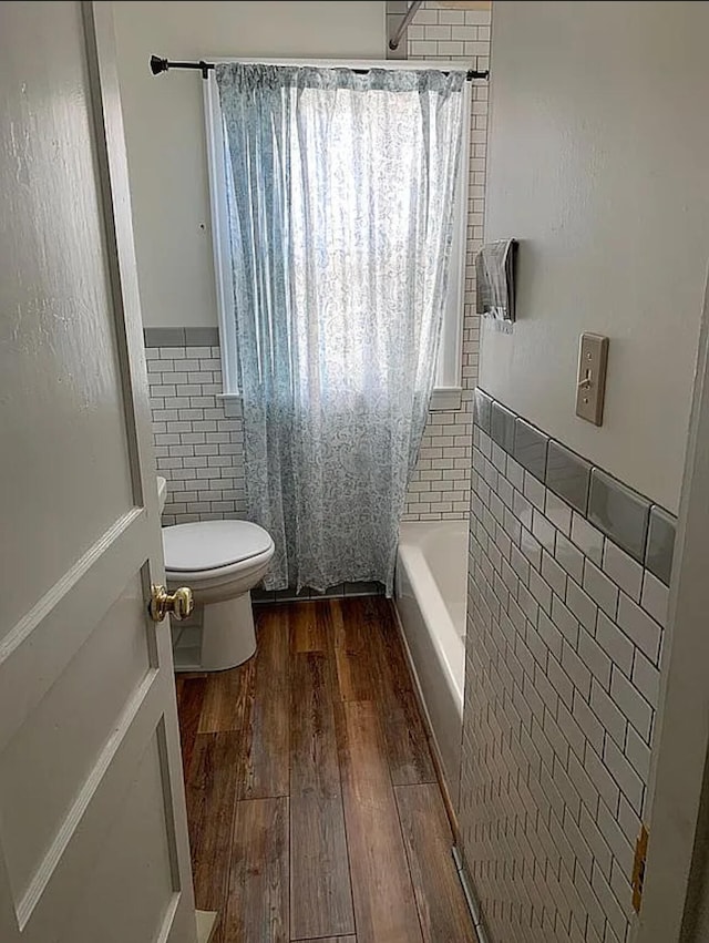 bathroom featuring hardwood / wood-style floors, toilet, tile walls, and shower / bathtub combination with curtain