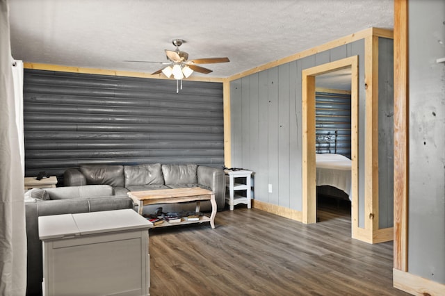 living room with ceiling fan, dark wood-type flooring, a textured ceiling, and wooden walls