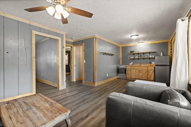 living room featuring a textured ceiling, dark wood-type flooring, wood walls, ornamental molding, and ceiling fan