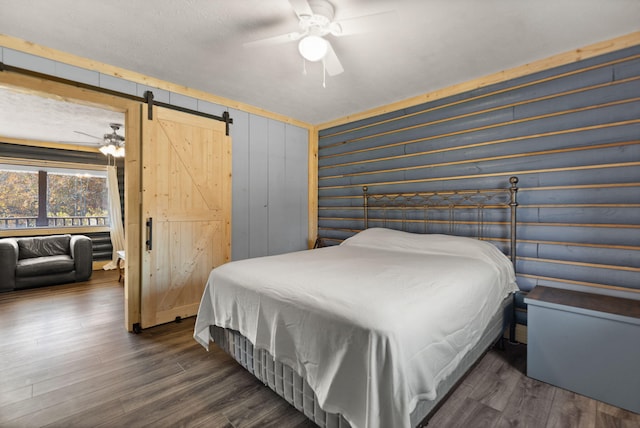 bedroom featuring ceiling fan, a barn door, dark hardwood / wood-style floors, and wooden walls