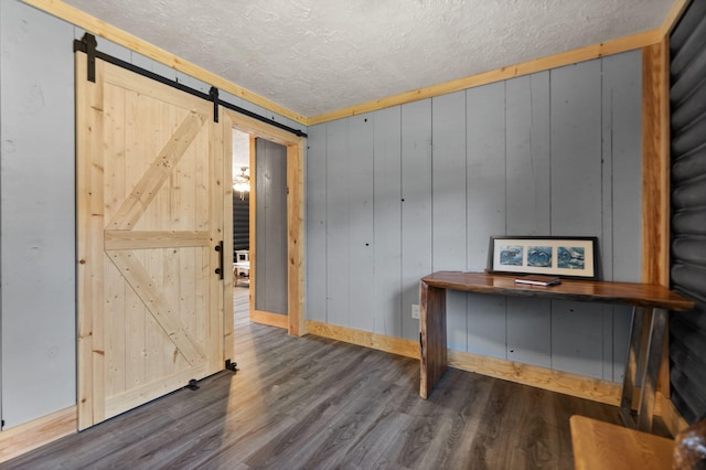 interior space with a textured ceiling, a barn door, hardwood / wood-style floors, and wooden walls