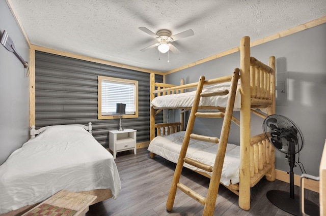 bedroom with ceiling fan, wood-type flooring, rustic walls, and a textured ceiling