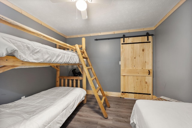 bedroom featuring ceiling fan, a barn door, dark hardwood / wood-style floors, and crown molding