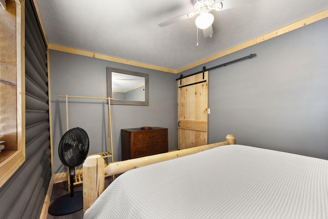 bedroom with ceiling fan, crown molding, and a barn door