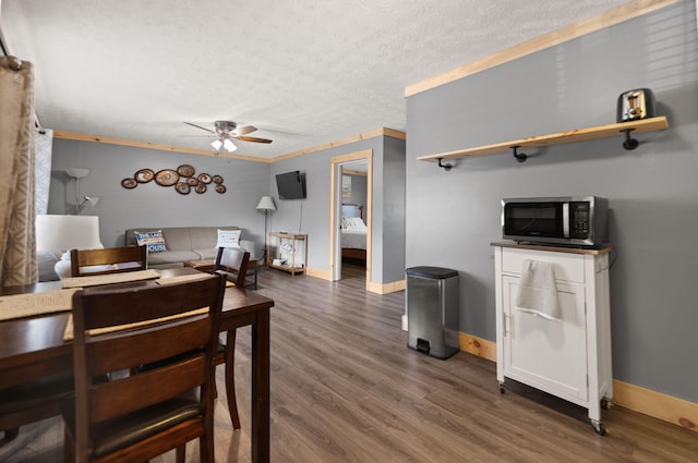 dining area with ceiling fan, dark hardwood / wood-style flooring, ornamental molding, and a textured ceiling