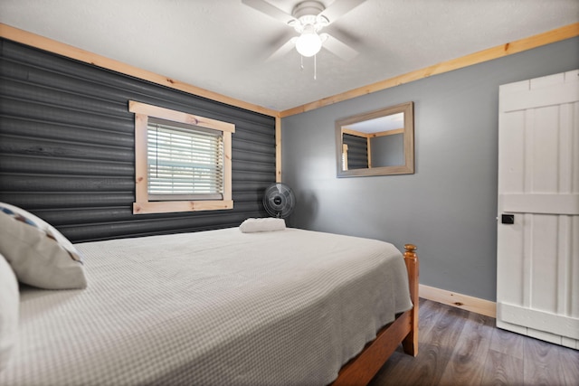 bedroom featuring dark wood-type flooring, ceiling fan, and log walls