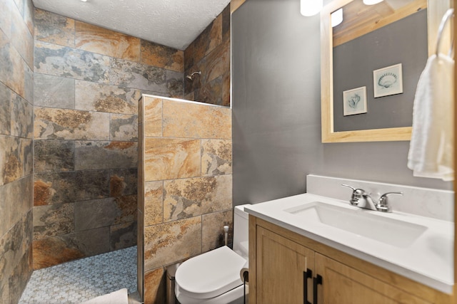 bathroom with a textured ceiling, tiled shower, vanity, and toilet