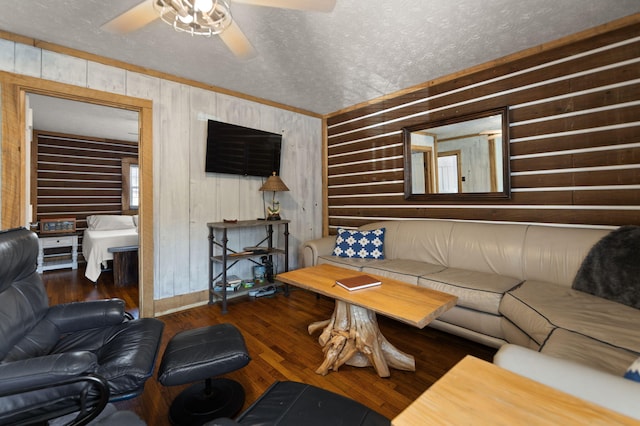 living room featuring ceiling fan, dark wood-type flooring, wood walls, and a textured ceiling