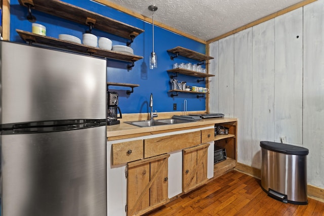 kitchen featuring dark wood-type flooring, stainless steel refrigerator, a textured ceiling, ornamental molding, and sink