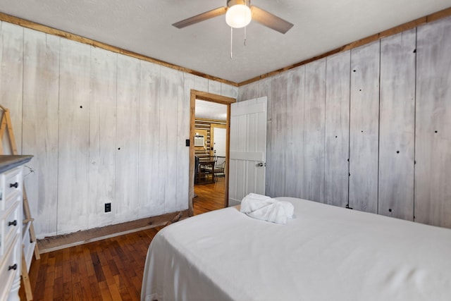 bedroom with ceiling fan, dark hardwood / wood-style floors, and wood walls