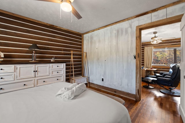 bedroom featuring ceiling fan, dark wood-type flooring, a textured ceiling, and wood walls