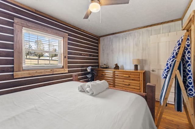 bedroom with ceiling fan, hardwood / wood-style floors, a textured ceiling, and wooden walls