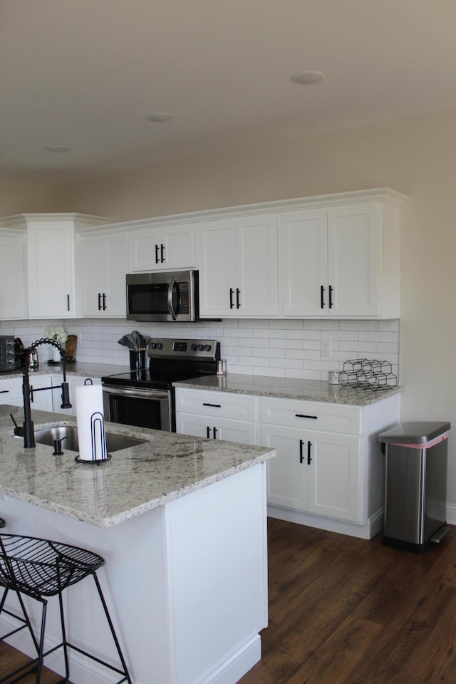 kitchen with dark wood-type flooring, white cabinets, backsplash, light stone countertops, and appliances with stainless steel finishes