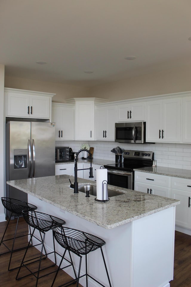 kitchen with stainless steel appliances, white cabinetry, dark hardwood / wood-style floors, sink, and a kitchen island with sink