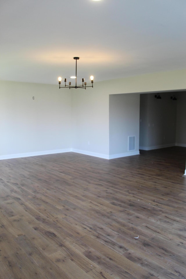 empty room with dark hardwood / wood-style floors and a notable chandelier