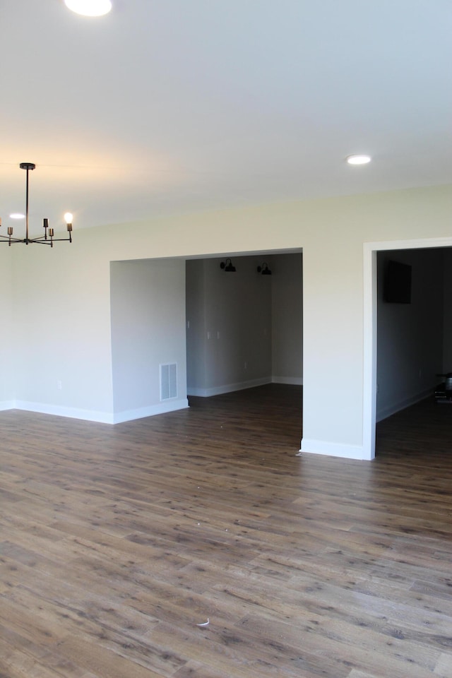 empty room with dark hardwood / wood-style flooring and a notable chandelier